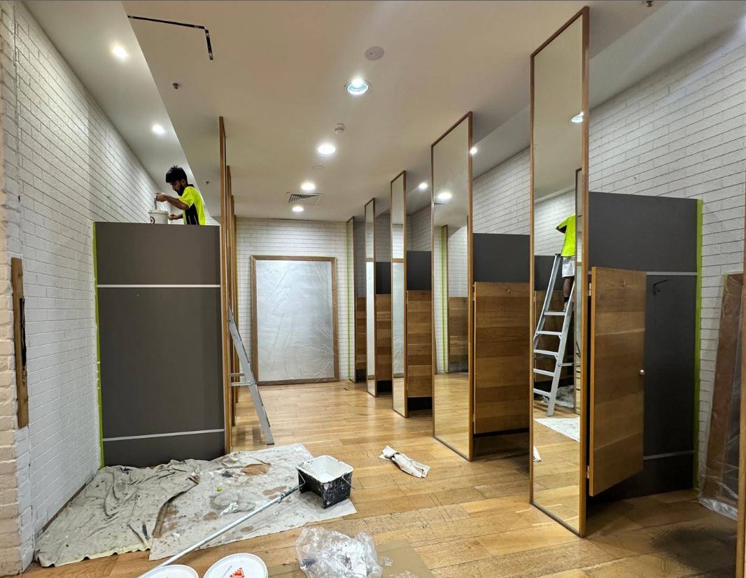 Commercial retail fit-out — painter on ladder finishing change-room partitions